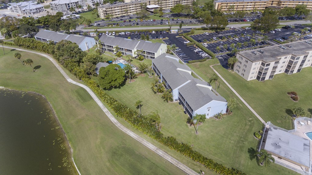 A large building sits in the middle of a grassy area with a parking lot in front.